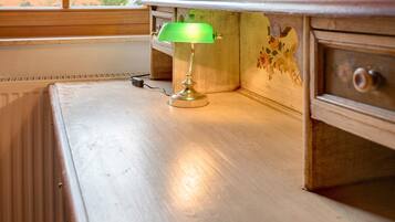 Uma luminária de mesa com cúpula verde sobre uma escrivaninha de madeira, perto de um radiador.