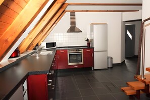 A modern kitchen with red cabinetry, a stainless steel oven, and a microwave.