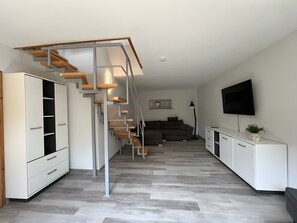 Ein moderner Wohnraum mit einer Holztreppe, weißen Schränken, einem Flachbildfernseher und einem Sofa.
