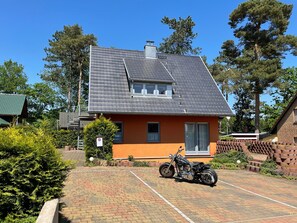 A house with a sloped roof, a parked motorcycle, and a paved driveway.