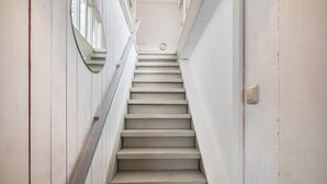 A narrow, white-painted stairway with a handrail on one side and a door on the other, leading to a landing with a circular window. - Holiday Home 'Atelierhaus Auf Hofjumne' with Private Terrace, Private Garden and Wi-Fi (Saal)