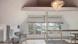 A room with a high ceiling, large windows, a chandelier, wicker furniture, and a view of the outdoors. - Holiday Home 'Atelierhaus Auf Hofjumne' with Private Terrace, Private Garden and Wi-Fi (Saal)