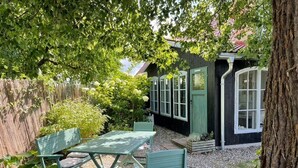 A garden with a table and chairs, a wooden structure with windows, and a tree. - Holiday Home 'Atelierhaus Auf Hofjumne' with Private Terrace, Private Garden and Wi-Fi (Saal)