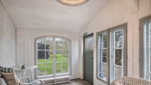 A room with white wooden walls, a large arched window, a green door, and wicker furniture. - Holiday Home 'Atelierhaus Auf Hofjumne' with Private Terrace, Private Garden and Wi-Fi (Saal)
