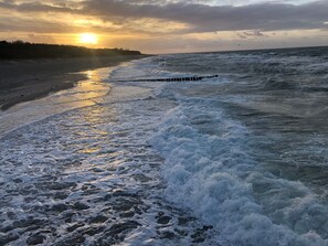 Une plage avec des vagues, une jetée en bois et un coucher de soleil.
