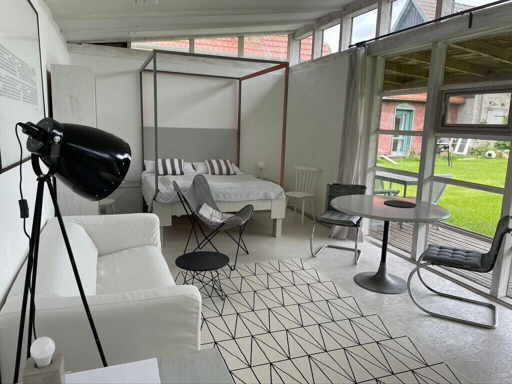 A modern bedroom with a four-poster bed, a white sofa, a small round table, and a large window with a view of a garden.
