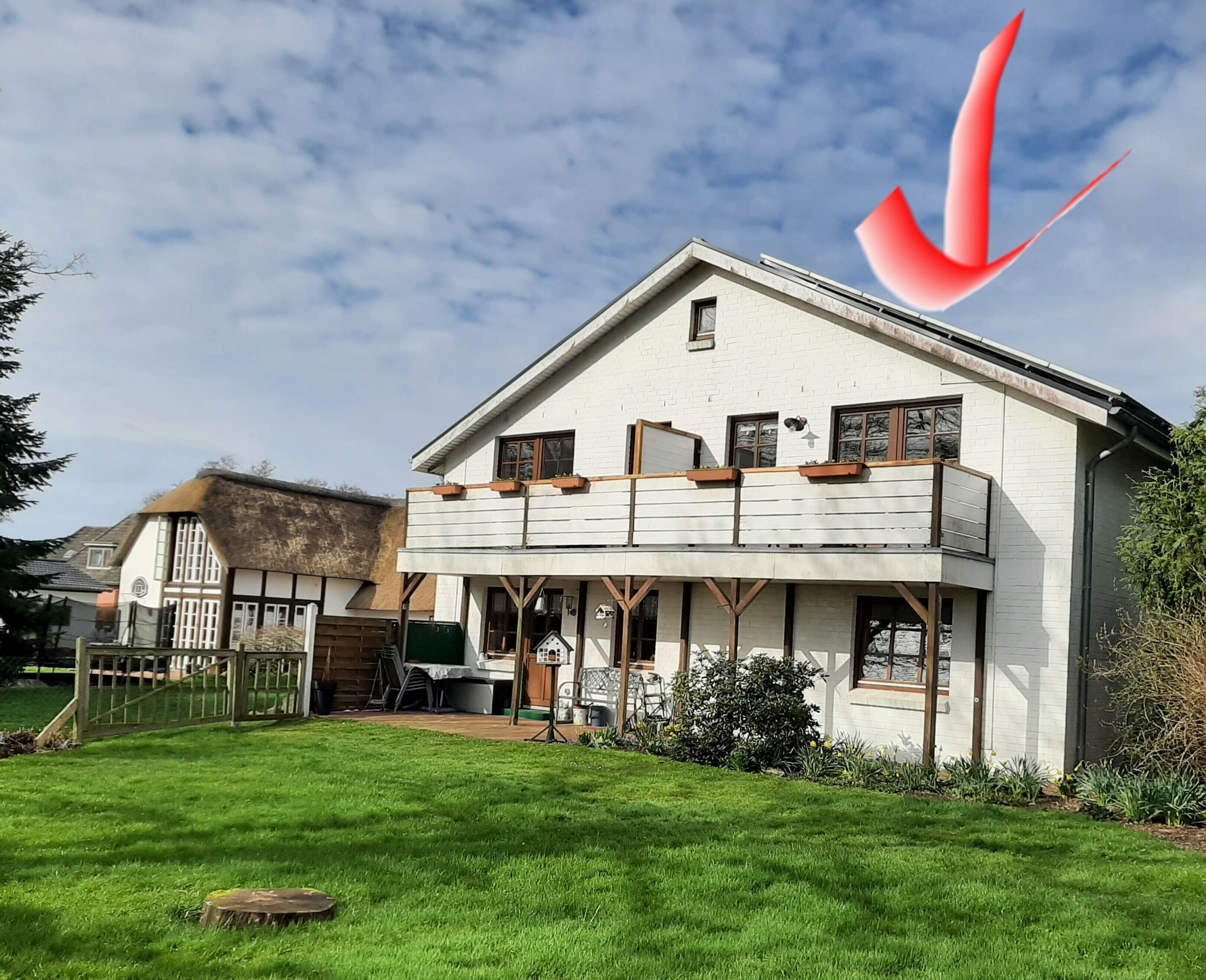 A two-story house with a balcony, a thatched roof, and a well-maintained lawn.