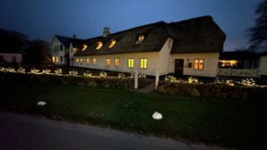 En stor, vit byggnad med många fönster och ett halmtak, omgiven av en stenmur och dekorerad med ljusslingor.