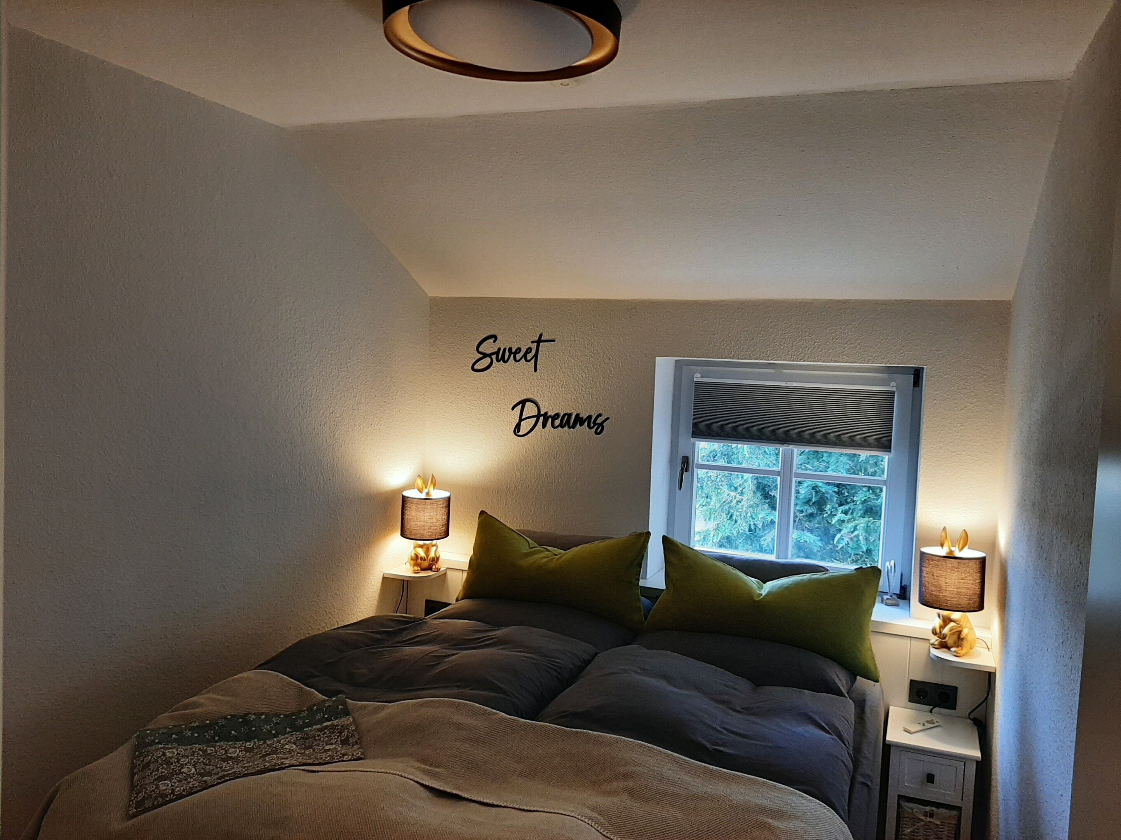 Une chambre à coucher avec un lit, deux lampes de chevet, une fenêtre et un mur sur lequel est écrit « Doux rêves ».