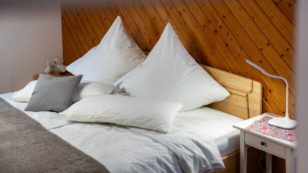 A neatly made bed with white and gray pillows, a wooden headboard, and a bedside table with a lamp.