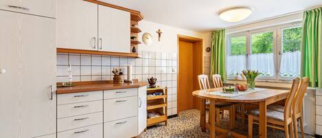 A kitchen with white cabinets, a wooden countertop, a tiled floor, a dining table with chairs, and a window with curtains.