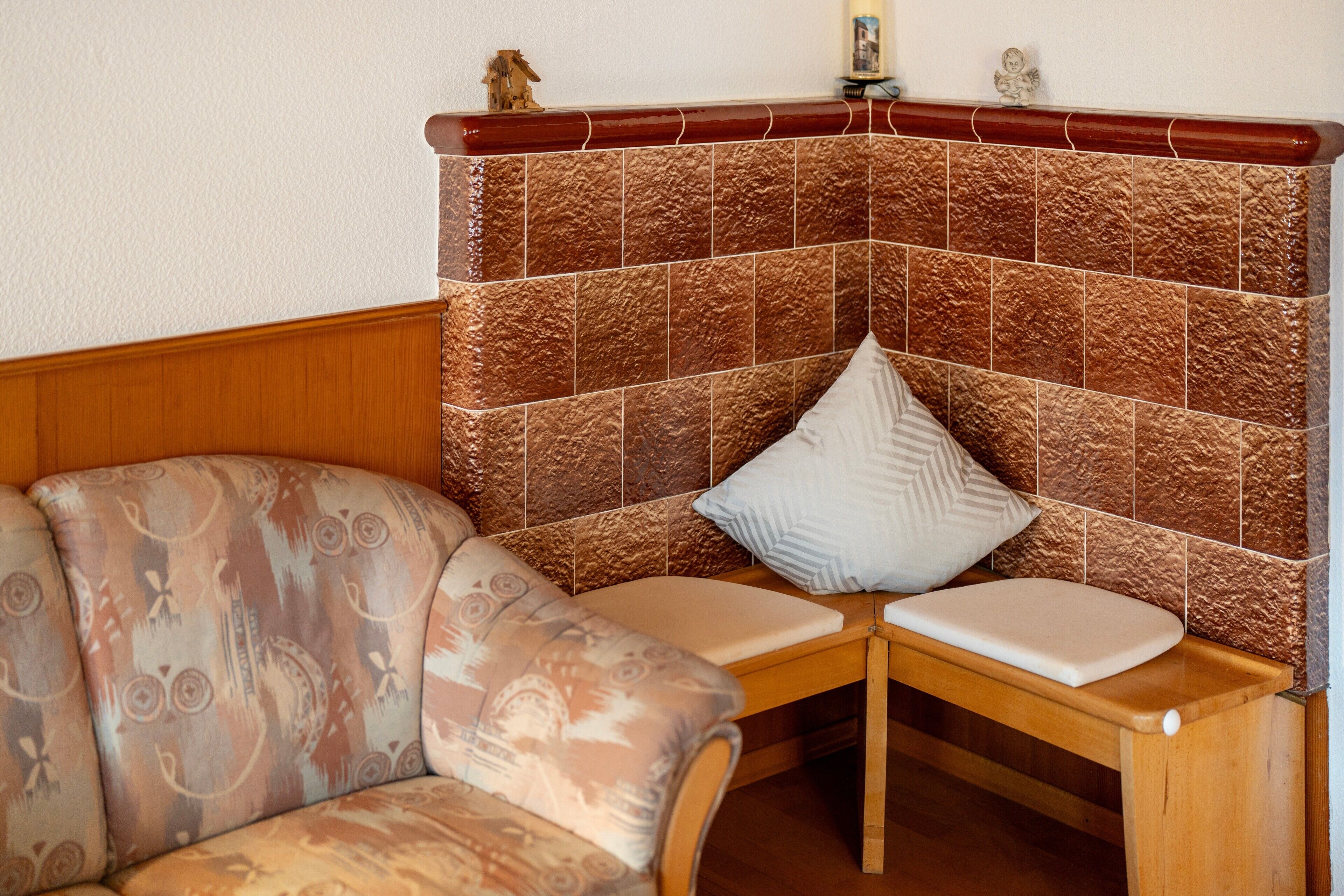 Un coin salon avec un banc rembourré et un canapé à motifs, un mur recouvert de carreaux et une petite étagère ornée d’objets décoratifs.