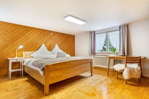 Une chambre à coucher avec un lit en bois, une table de chevet, une chaise et une fenêtre avec des rideaux.