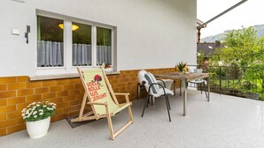 A balcony with a wooden chair, a table, and a potted plant.