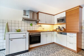 Une cuisine avec des meubles blancs, un four à micro-ondes, un four traditionnel et un lave-vaisselle.