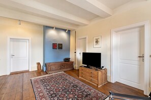 A room with hardwood floors, a patterned rug, a wooden dresser with a flat-screen TV, and a door with a white frame.