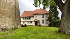Une maison à deux étages, avec un toit recouvert de tuiles rouges, une porte d’entrée et un petit jardin devant.