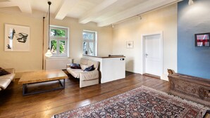 Un salon spacieux avec une table basse en bois, un canapé, un petit bureau blanc et un tapis à motifs.