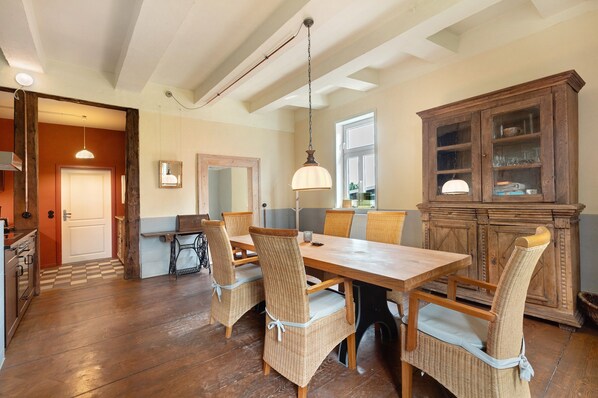 A dining area with a wooden table and chairs, a hanging light fixture, and a wooden cabinet with glass doors.