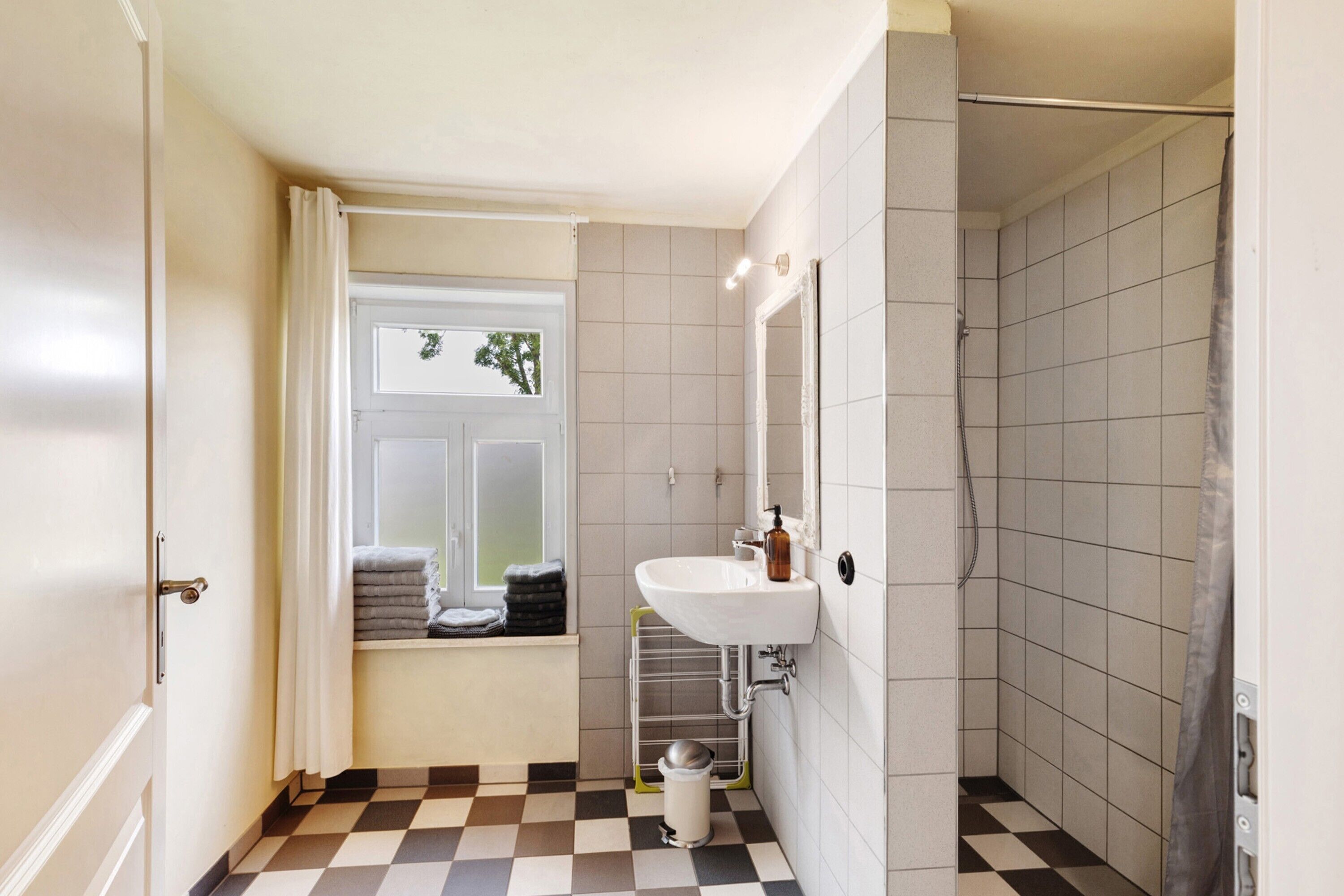 Un baño con piso a cuadros, un lavamanos, una ventana con vistas y una zona de ducha.