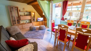 Una sala de estar acogedora con un sofá, un televisor, un comedor con sillas y una mesa, y una ventana con cortinas.