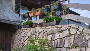 Un muro de piedra con una escalera de madera, plantas en macetas y una terraza de madera.