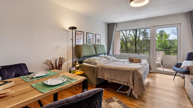 Une chambre à coucher moderne avec un lit, une table de chevet, une lampe et une vue sur l’extérieur.