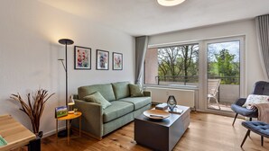 Un salon moderne avec un canapé, une table basse et une vue sur l’extérieur grâce à de grandes fenêtres.
