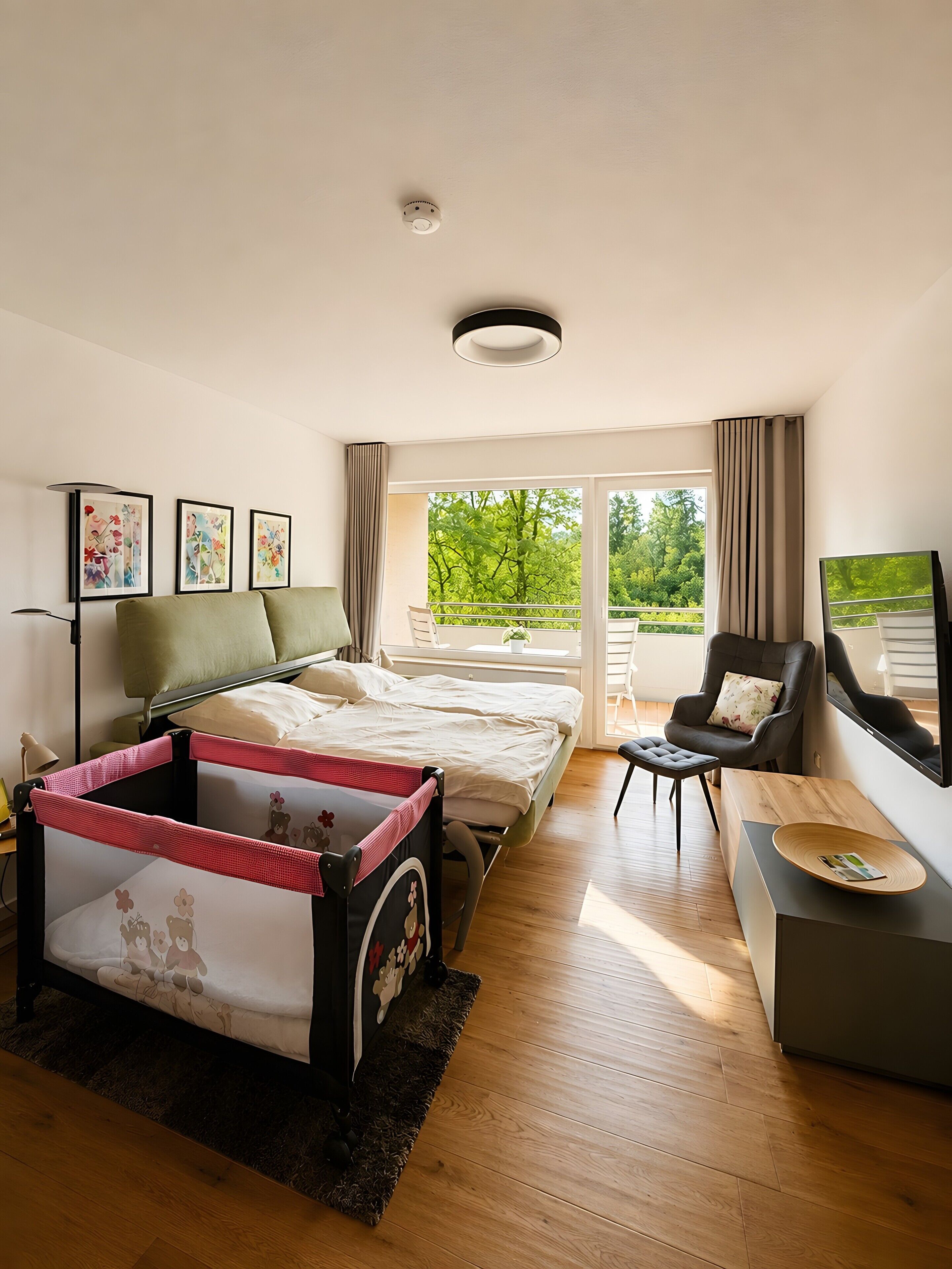 A modern bedroom with a bed, a desk, a chair, and a balcony with a view of greenery.