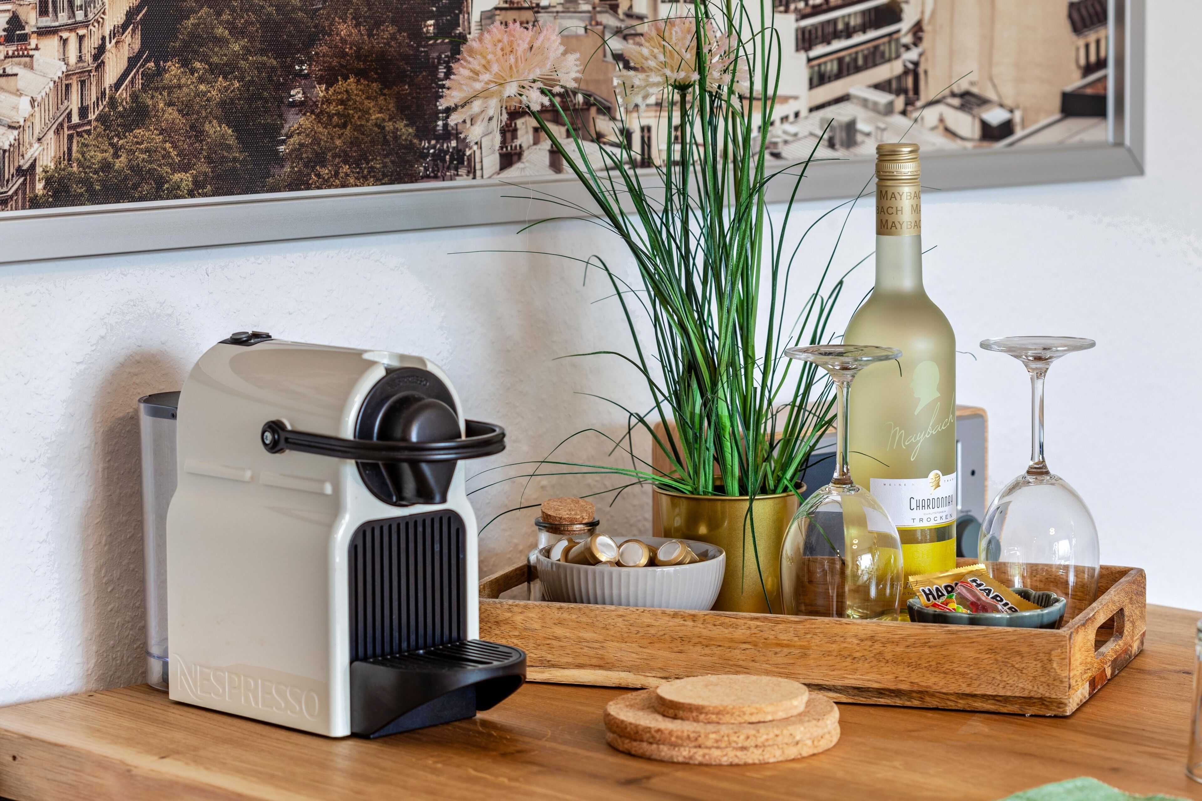 A Nespresso machine, a bottle of Chardonnay, a glass, a plant, and a tray with snacks.