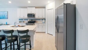 A modern kitchen with white cabinets, a stainless steel refrigerator, a microwave, and a large island with bar stools. - Relaxing coastal home centrally located in Port Charlotte - Fireside Cottage (Port Charlotte)