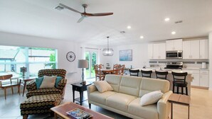 A modern living room with a sofa, armchair, and coffee table. There is a dining area with chairs and a table, and a kitchen with cabinets and appliances. - Relaxing coastal home centrally located in Port Charlotte - Fireside Cottage (Port Charlotte)
