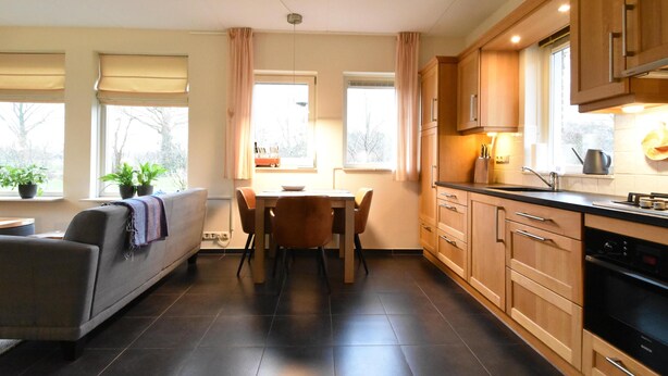 A modern kitchen with wooden cabinets, a Bosch oven, and a dining area with a table and chairs. - Rural apartment with garden (Zuidwolde)