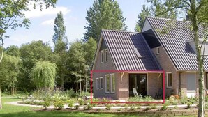 A two-story house with a sloped roof, a brick exterior, and a front porch with a chair. - Rural apartment with garden (Zuidwolde)