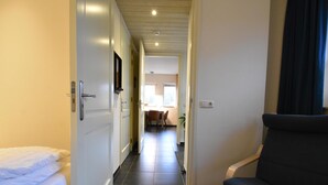 A hallway with a bed, a chair, and a view into a dining area. - Rural apartment with garden (Zuidwolde)