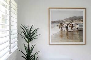 A framed beach scene with a plant beside a window.