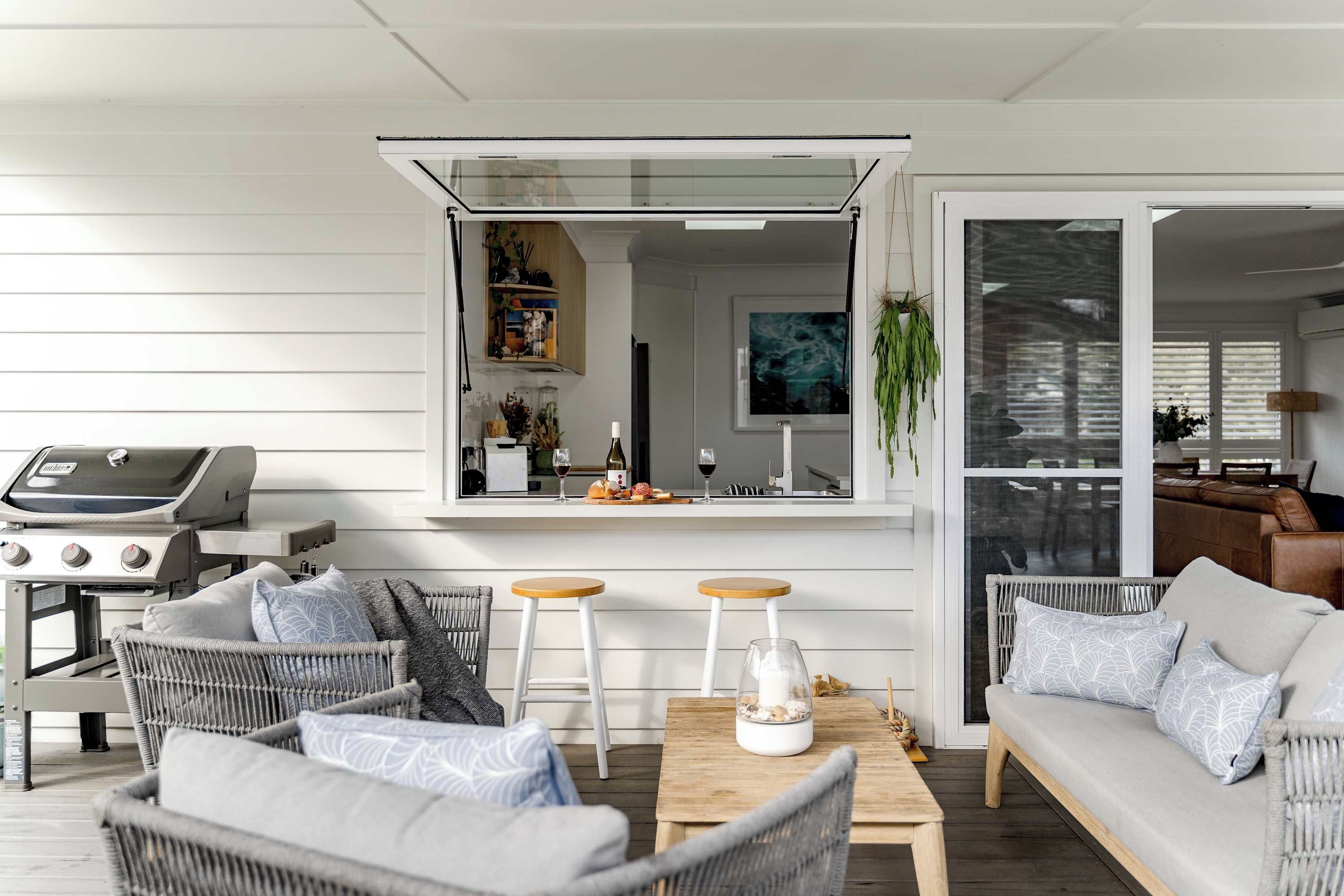 A modern outdoor seating area with wicker furniture, a wooden table, and a grill.