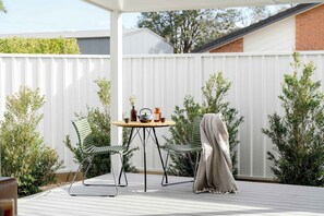 A deck with a table and chairs, a covered area, and a white fence.