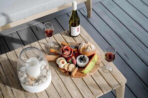 A wooden table with a charcuterie board, a bottle of wine, and two glasses of red wine.