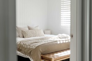 A bedroom with a bed, pillows, a bedside table, and a window with blinds.