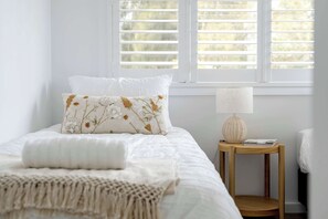 A bedroom with a bed, a bedside table with a lamp, and a window with blinds.