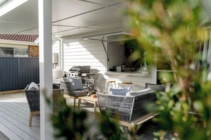 A covered outdoor patio with wicker furniture, a barbecue grill, and a view of a house in the background.