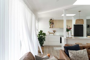A modern living room with a brown leather sofa, a coffee table, and a large window with sheer curtains.