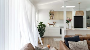 A modern living room with a brown leather sofa, a coffee table, and a large window with sheer curtains.