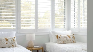 A bedroom with two beds, white bedding, and a small bedside table with a lamp.