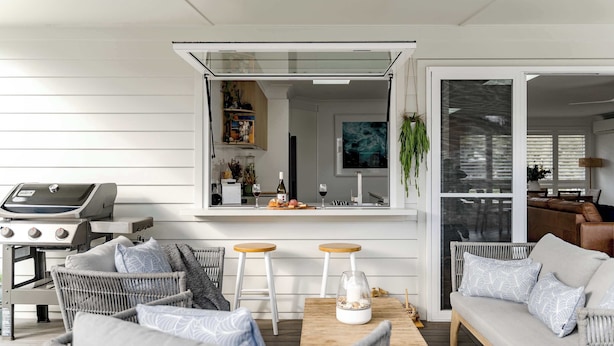 A modern outdoor seating area with wicker furniture, a wooden table, and a grill.