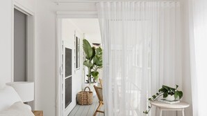 A minimalist bedroom with a large bed, a small side table, and a view of a balcony with plants. - The Cali Jervis Bay (Vincentia)