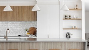 A modern kitchen with a central island, wooden stools, white pendant lights, and a stone backsplash. - The Cali Jervis Bay (Vincentia)