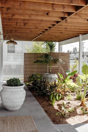 A covered outdoor area with a wooden ceiling, a white fence, and various potted plants. - The Cali Jervis Bay (Vincentia)