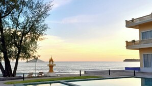 A pool area with a clear view of the sea and a building with a balcony.